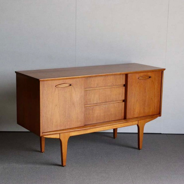 Mid-century British vintage teak sideboard by Jentique with smooth wood grain, tapered legs, two cupboards, and three.