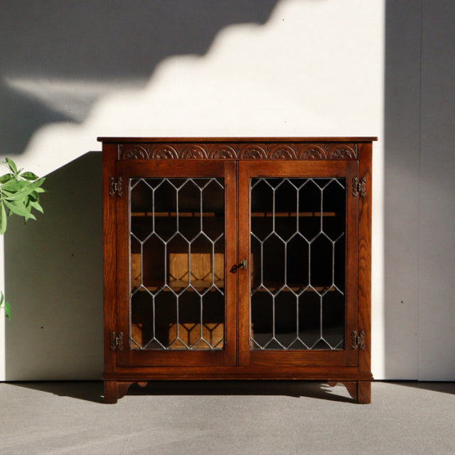 Vintage teak cabinet by Jaycee featuring British mid-century design with detailed carved top, leaded glass doors, and sturdy .