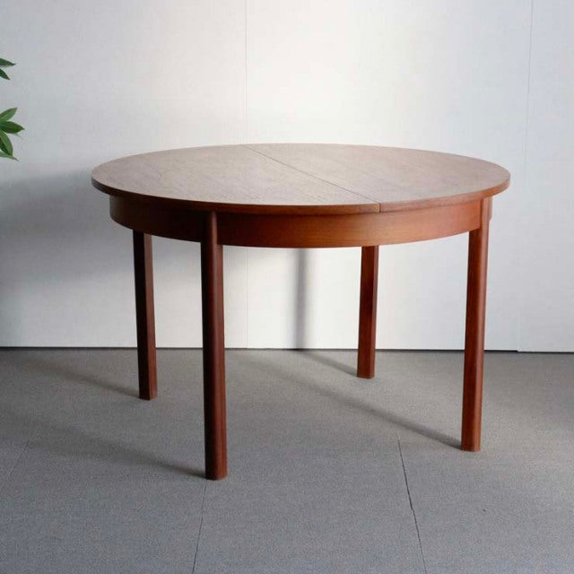 Mid-century British vintage teak dining table with round top, extending feature, and slender tapered legs.