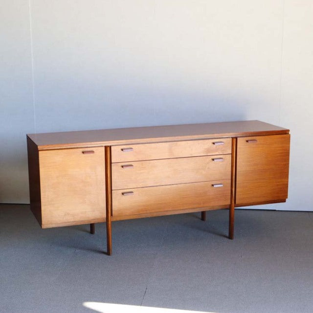 Vintage teak British mid-century sideboard with smooth wood grain, three central drawers, and flanking cabinets on slender.
