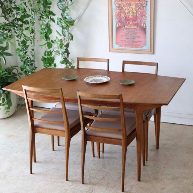 Vintage British mid-century teak dining table with rectangular top and matching chairs, slender tapered legs, smooth wood.