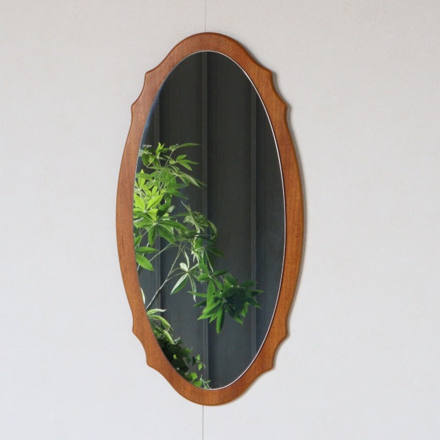 Mid-century British vintage teak wall mirror with oval shape and decorative carved frame edges.