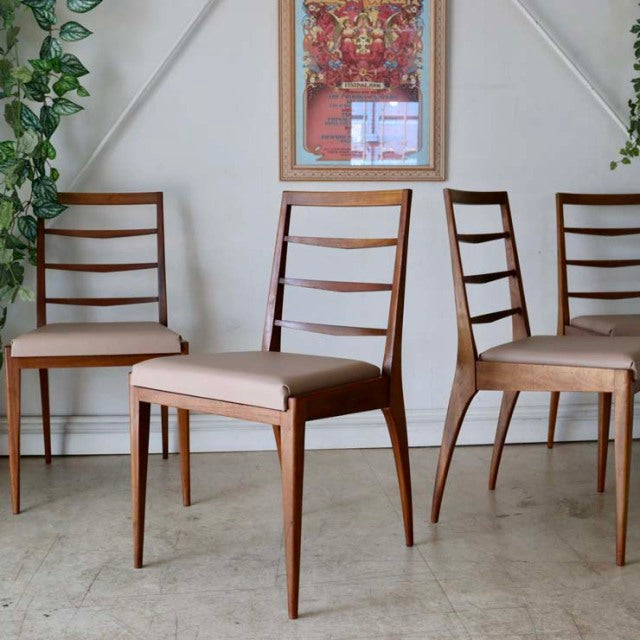Set of four vintage mid-century teak dining chairs with sleek ladder backs and tapered legs, showcasing smooth wood grain.