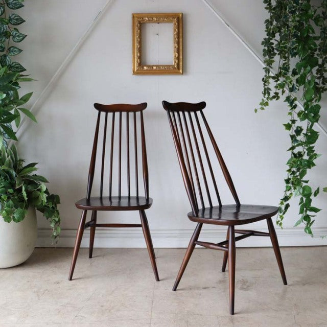 Pair of vintage ERCOL Goldsmith highback Windsor chairs in teak with slender spindle backs, tapered legs, and smooth curved.