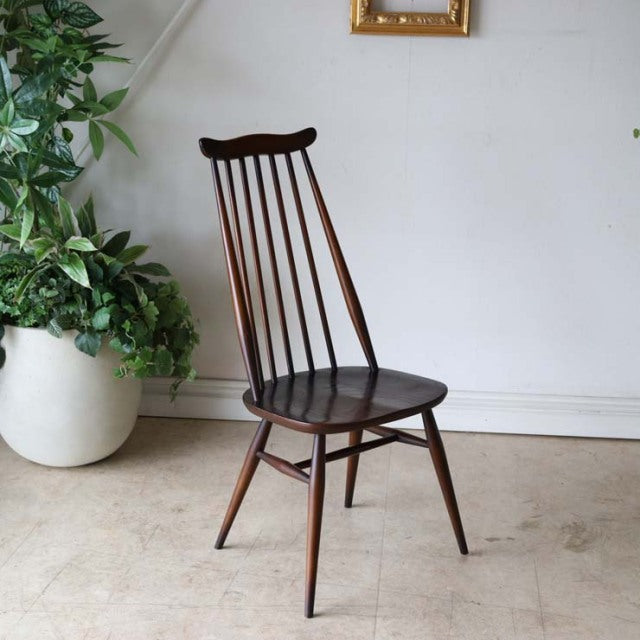 British mid-century Ercol Goldsmith dining chair in dark teak with slender spindle back and tapered legs.
