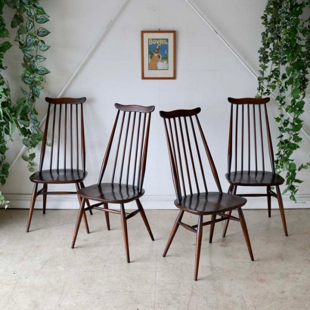 Four vintage British Ercol Goldsmith high-back dining chairs in teak with slender vertical spindle backs and angled legs,.