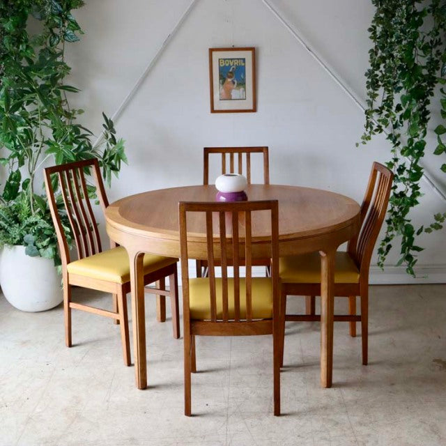 Vintage teak round dining table with mid-century British design, accompanied by four matching teak chairs with vertical slat .
