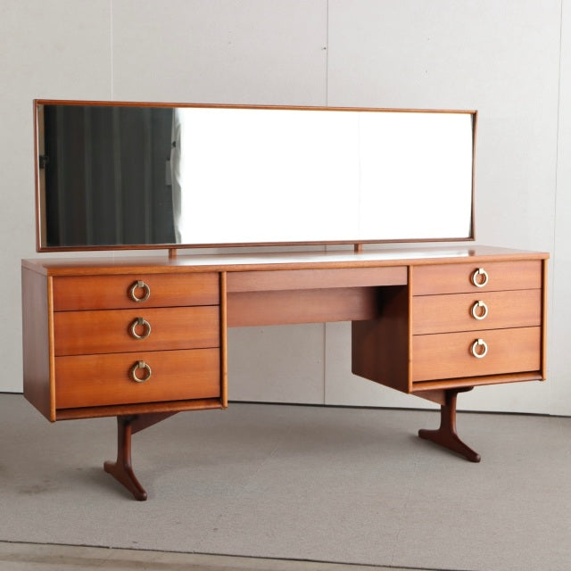 Mid-century British AustinSuite teak dresser with wide rectangular mirror, six drawers, and sleek angled legs showcasing.