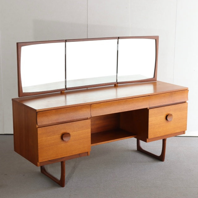 Mid-century British vintage teak dressing table with three-panel mirror, rounded drawer handles, and tapered legs from.