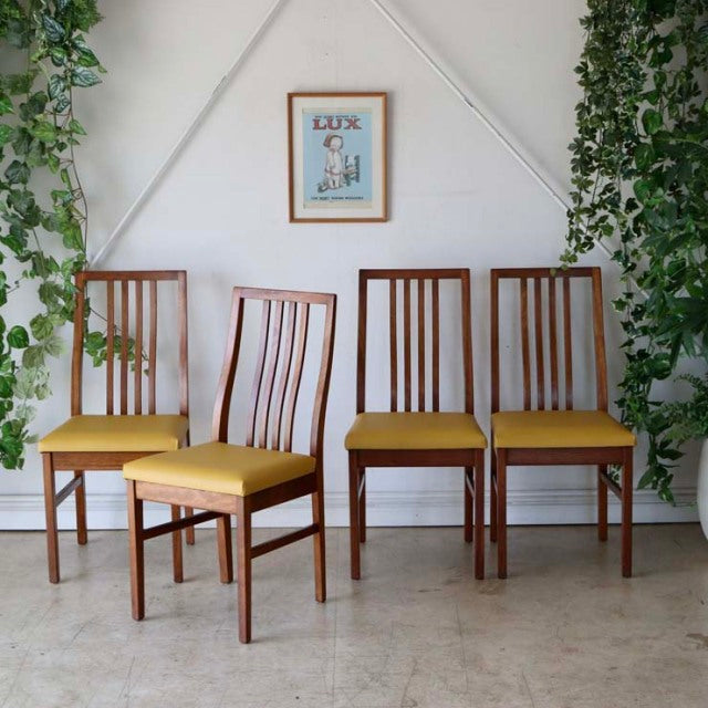 Set of four vintage British mid-century teak dining chairs with yellow upholstered seats, slim vertical slat backs, and.