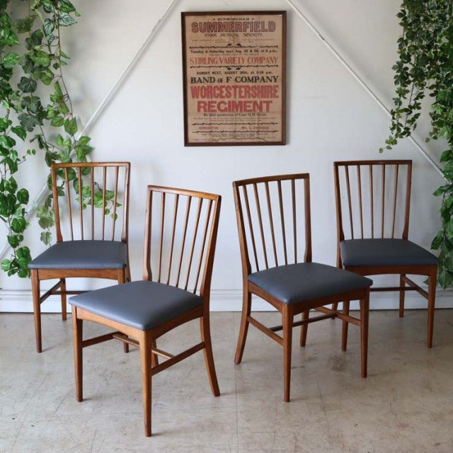 Set of four vintage British mid-century teak dining chairs with slender vertical slat backs and dark upholstered seats in.