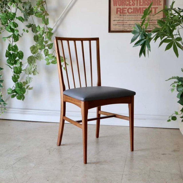 Vintage mid-century British teak dining chair with sharp backrest, vertical slats, and black upholstered seat, set against a .
