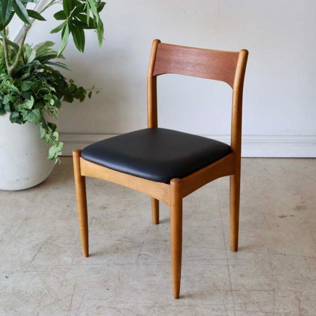 Mid-century British vintage teak dining chair with sleek black cushioned seat and tapered legs.