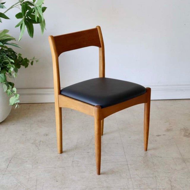 Vintage mid-century teak dining chair with black cushioned seat, sleek British-Denmark design, and angled legs featuring.