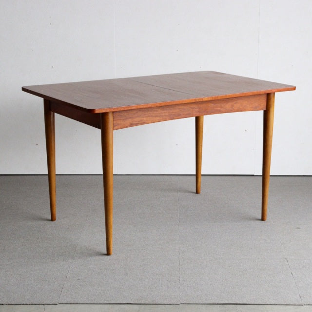 Mid-century British vintage teak dining table with rectangular top and tapered legs, smooth wood grain visible.