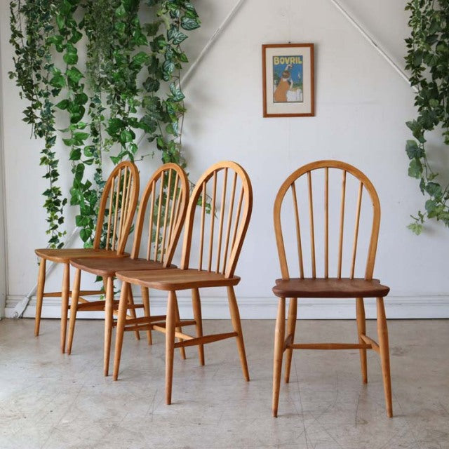 Set of four British mid-century ERCOL dining chairs in vintage teak with spindle hoopback and X-back designs, showcasing.